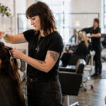 Prospective cosmetology student observing a hairstylist section a client's hair during a normal busy day in a professional salon.